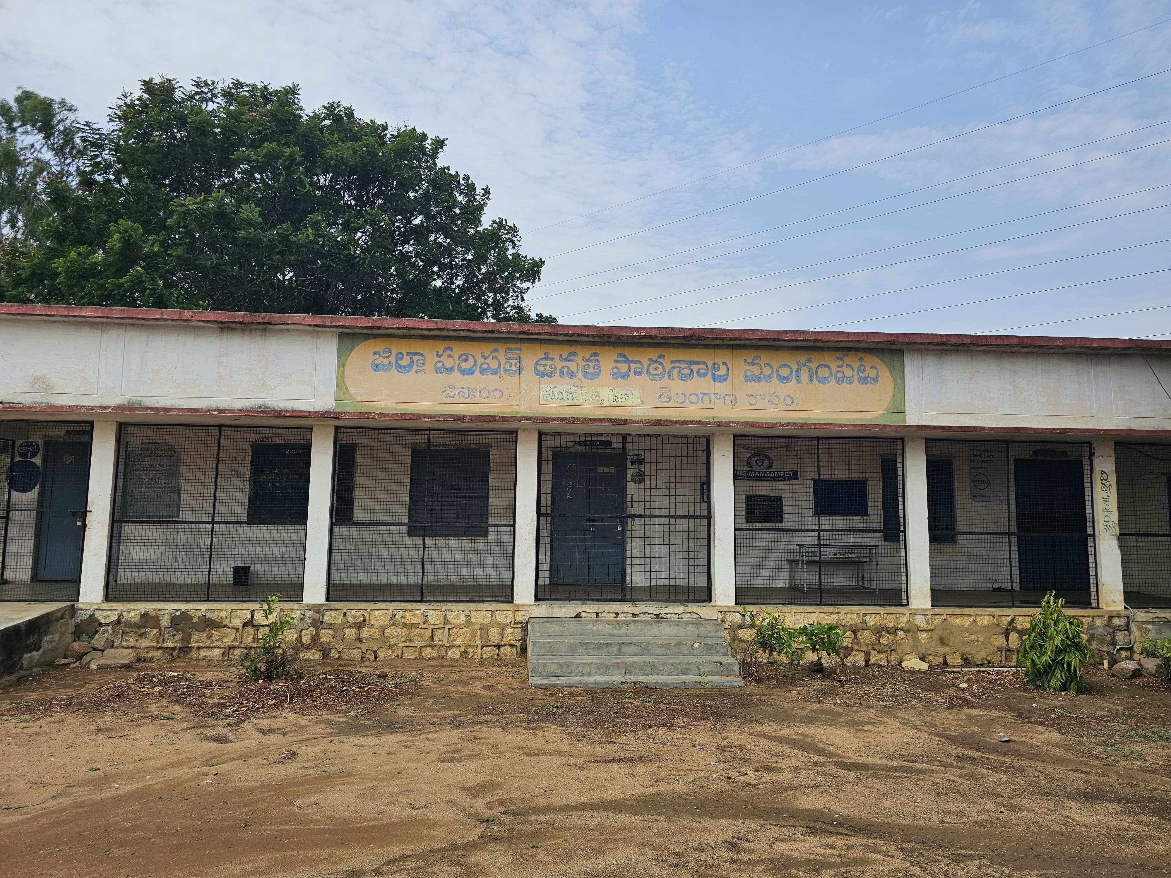 An view of the Jinnaram ZPHS campus in Telangana: the main classroom block, open courtyard, and entrance gate.